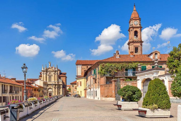Promenade along old colorful houses and church under blue sky in town of Bra in Piedmont, Northern Italy.