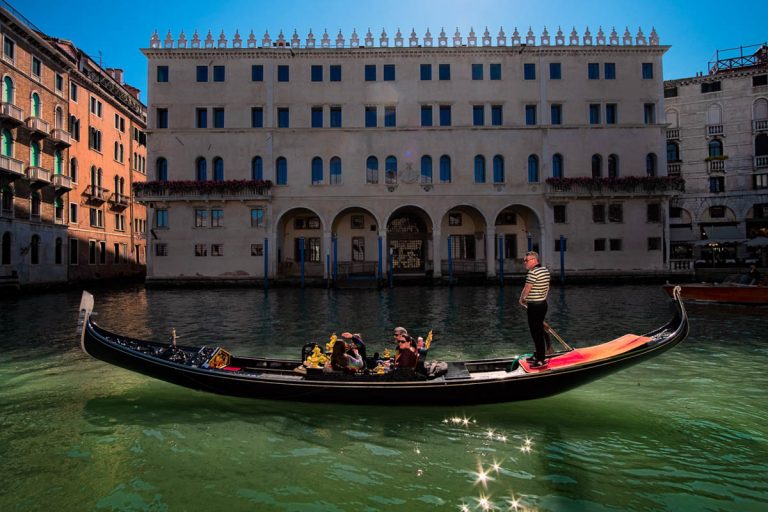 Italy, Venice - April 2019. A gondolier floats on a canal at the Rialto Bridge with passengers opposite the center of T Fondaco dei Tedeschi by DFS.