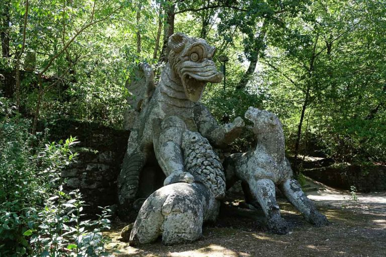 Bomarzo, Viterbo, Lazio, Italy - 08.25.2020: The large statue of the Dragon bitten by a lion and a dog at the famous Parco dei Mostri, also called Sacro Bosco or Giardini di Bomarzo. Monsters park