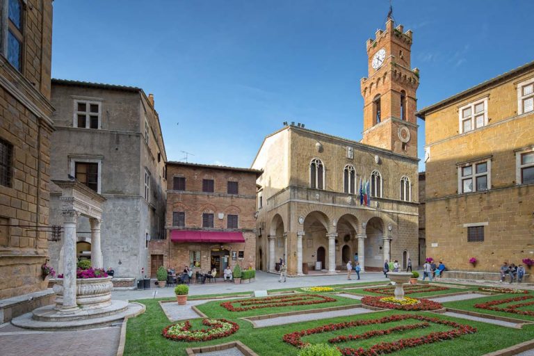 Pienza, Tuscany/Italy - May 10 2016: Piazza Pio II., Idyllic square with fountain, town hall and a small coffee house in Pienza. Tourists and local people on the Piazza in the old town of Pienza